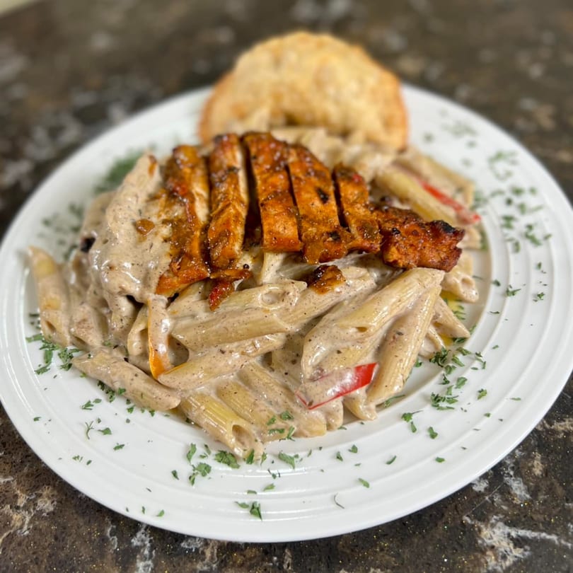 Penne pasta in a creamy sauce topped with sliced grilled chicken and a side of bread.