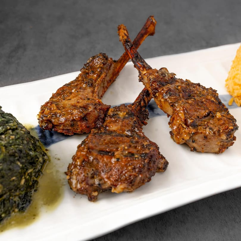 Grilled lamb chops with a side of green spinach and yellow rice on a white plate.