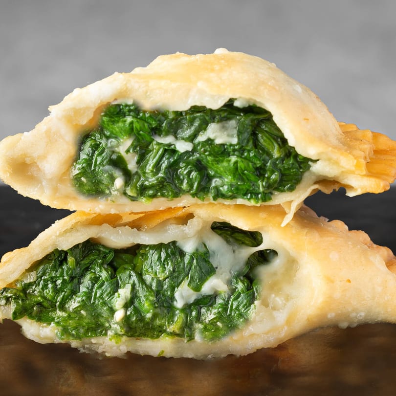 Two Supreme Empanadas, cut in half, revealing a vibrant spinach and cheese filling.