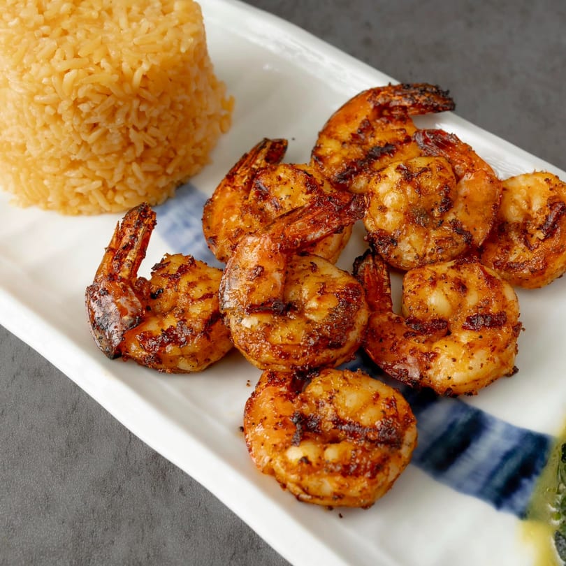 Grilled shrimp and a mound of yellow rice on a white rectangular plate with blue accents.