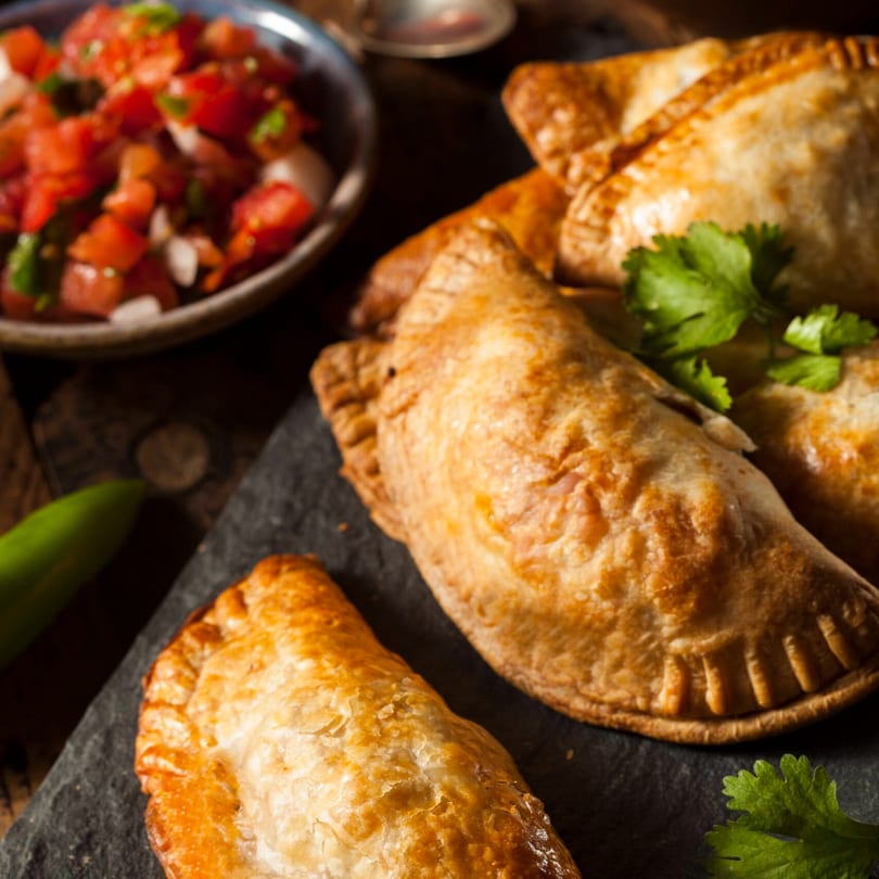 Golden-brown Supreme Empanadas on a dark slate with fresh salsa and cilantro.